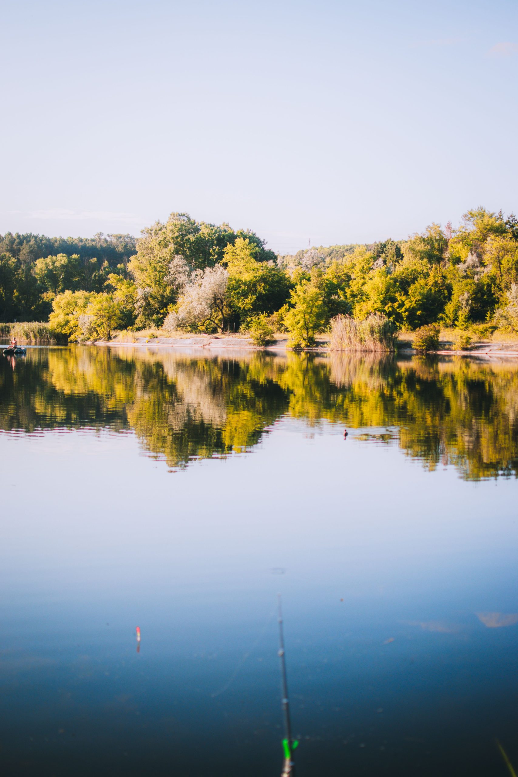 A fishing rod over a calm lake surrounded by trees