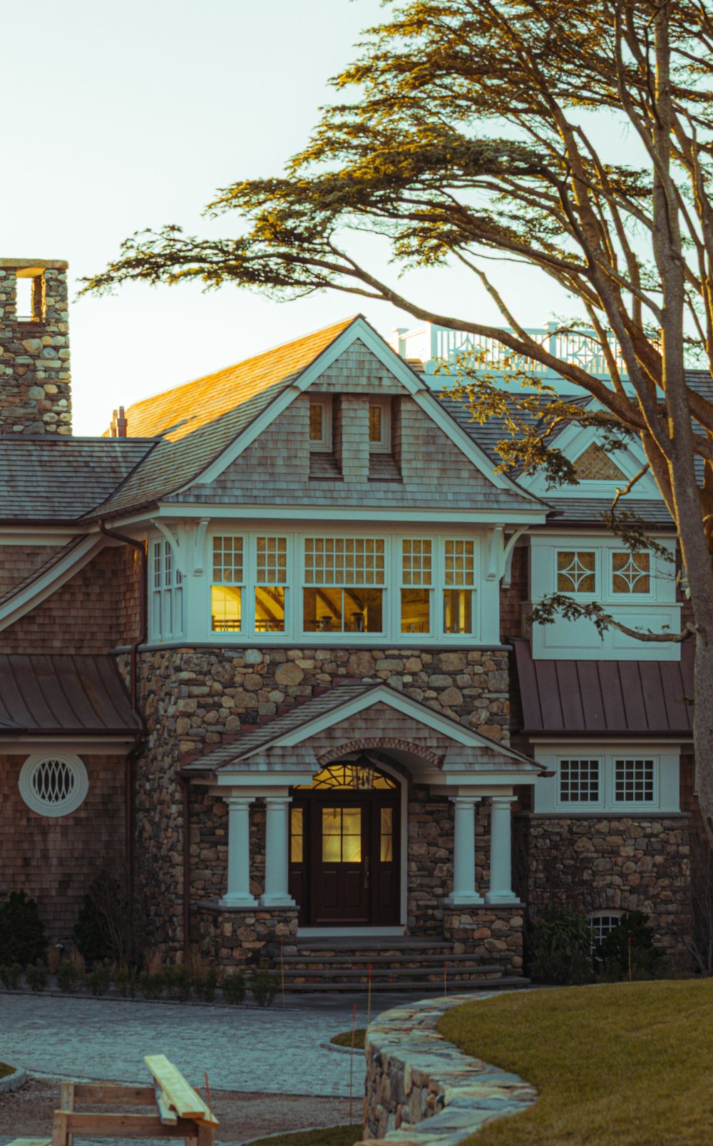 Stone and shingle-style estate entrance with columned portico and gambrel roofline